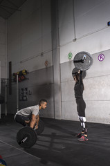 Motivational wide shot of young man and woman holding barbells overhead