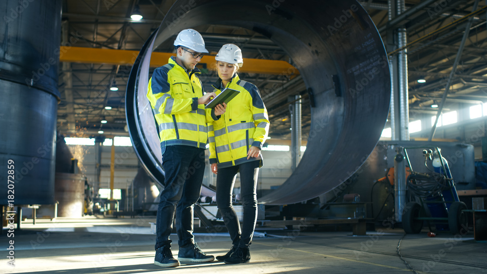 Poster male and female industrial engineers in hard hats discuss new project while using tablet computer. t