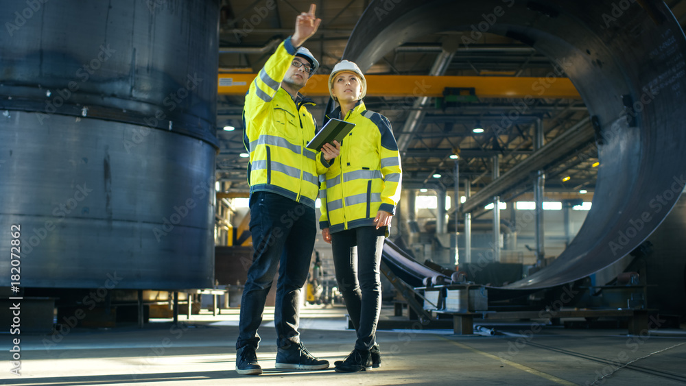 Poster male and female industrial engineers in hard hats discuss new project while using tablet computer. t