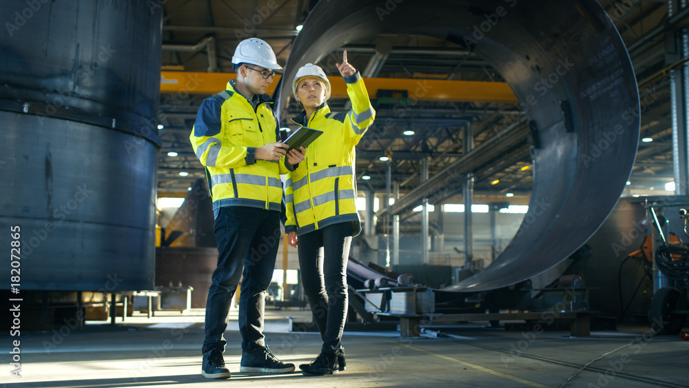 Poster male and female industrial engineers in hard hats discuss new project while using tablet computer. t