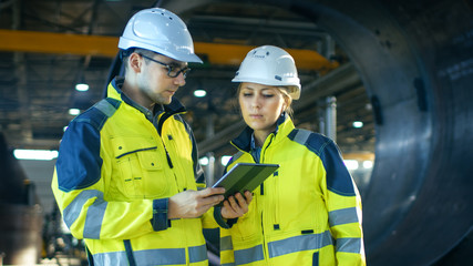 Male and Female Industrial Engineers in Hard Hats Discuss New Project while Using Tablet Computer....