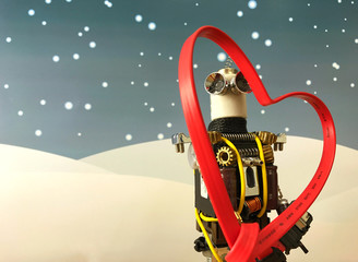 Closeup image of robot having big red heart in hand made of cable with Christmas background. Snow falling down and robot standing.
