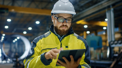 Industrial Engineer in Hard Hat Wearing Safety Jacket Uses Touchscreen Tablet Computer. He Works at...
