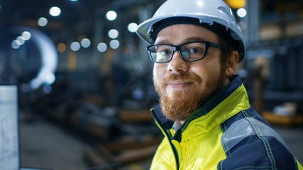  Industrial Engineer Wearing Hard Hat,  Safety Jacket and Glasses Smiles on Camera. He Works in Big...