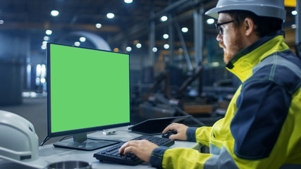 Inside the Heavy Industry Factory Industrial Engineer Works on the Personal Computer with Green...