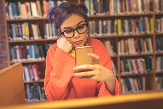 Woman using mobile phone while reading book in library