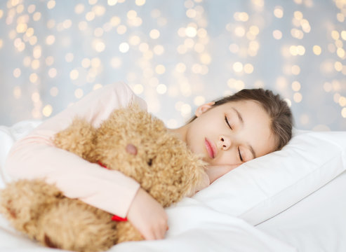 girl sleeping with teddy bear toy in bed