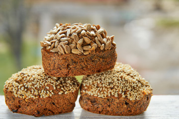Three freshly baked raisins cakes with sesame and sunflower seeds isolated on white wooden table. Three healthy vegetarian muffins on blurred nature background. Side view