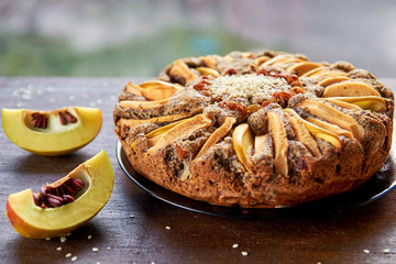 Apple tart with quince, poppy seeds, raisins and sesame on wooden brown table. Apple pie decorated with sliced fresh quince and sesame seeds on the blurred background. Side view 