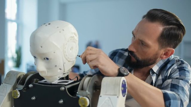 No spare moment. Close up of qualified engineer using a screwdriver while being focused on repairing robots head