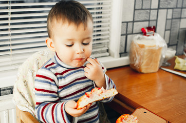 The little boy in the kitchen eating a small pizza