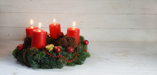 Advent wreath with four red burning candles and christmas decoration on rustic white wood, panorama...