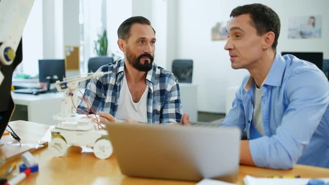 Sharing thoughts. Optimistic constructors sitting at the table while using a laptop and having exciting discussion about work issues