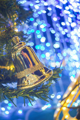 blur image of  bell  hang on the fake pine Christmas tree. The background is blue light and bokeh.