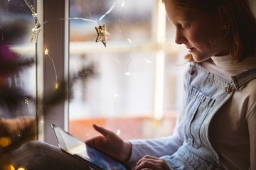 Girl sitting near window and using digital tablet at home