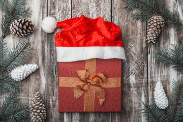 Old wooden background. Fir branches, cones. Christmas Fellowship, New Year and Xmas. A red gift in the center. Holiday card. Santa's Cap.Xmas and Happy New Year composition. Flat lay, top view