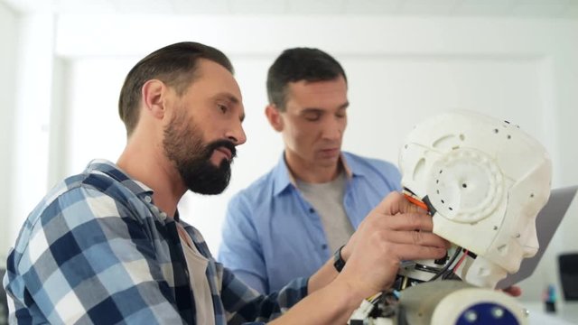 Targeted at working. Close up of smart enthusiastic constructors repairing robot head while being attentive
