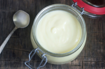 Custard vanilla cream in a glass jar on a wooden background.