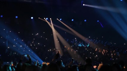 Concert hall with viewers. Audience watching concert on stage in big concert club. Cheering crowd in concert hall. Viewers move in time with the music. Audience is shining with flashlights of phones. - Powered by Adobe