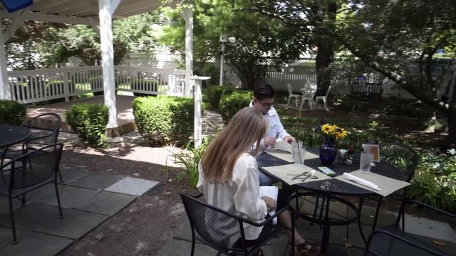 Camera revolves around a mature mother and hipster teen son sitting at an outdoor table waiting for their lunch or dinner to be delivered.