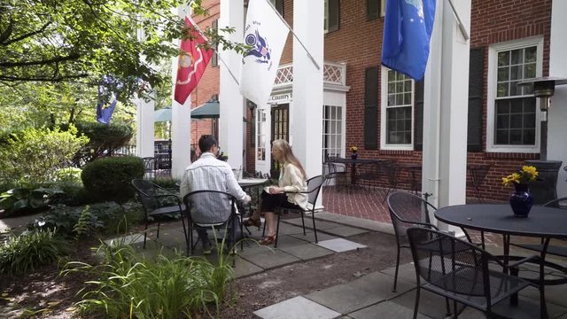 Camera revolves around a mature mother and hipster teen son sitting at an outdoor table waiting for their lunch or dinner to be delivered.