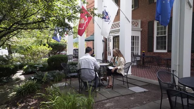 Camera moves around a mature mother and hipster teen son sitting at an outdoor table waiting for their lunch or dinner to be delivered.