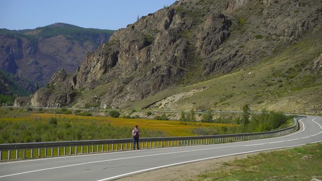 Young traveler man with backpack walking alone on the road on the mountain. Hitchhiker on a road. Travel. 4 k