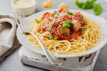 Pasta spaghetti with tomato sauce, parmesan cheese, basil and meatballs on white ceramic plate on gray concrete or stone background. Selective focus. Top view.