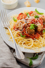 Pasta spaghetti with tomato sauce, parmesan cheese, basil and meatballs on white ceramic plate on gray concrete or stone background. Selective focus. Top view.
