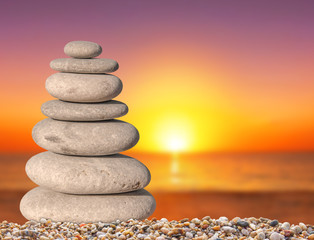 Obraz na płótnie Canvas Small beach zen stone with sun down background close up for spa and balance symbol