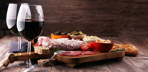 Italian antipasti wine snacks variety set. Cheese, Mediterranean olives, pickles, Prosciutto di Parma, tomatoes, artichokes and wine in glasses. Spanish tapas.
