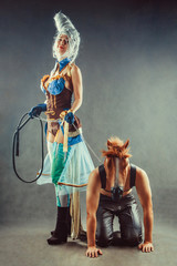 Young couple in a role playing game, girl is holding a man in the horse mask on the chain.