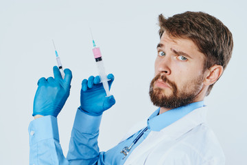 Man with a beard on a light background in a medical uniform holds syringes, doctor, medicine