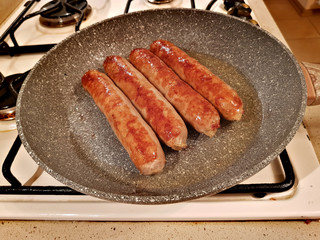 Appetizing ruddy juicy sausages fried in a large frying pan
