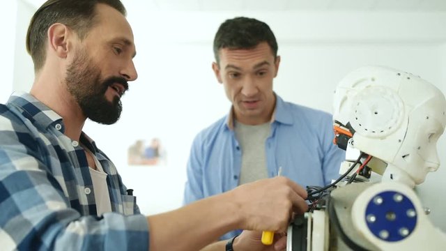 Working hours. Close up of enthusiastic constructors standing near robot mockup and having exciting discussion about further engineering plan