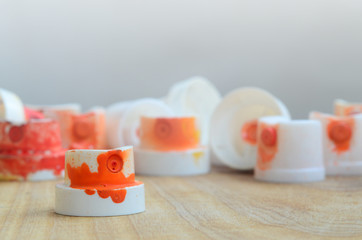 Several plastic nozzles from a paint sprayer that lie on a wooden surface against a gray wall background. The caps are smeared in orange paint. The concept of street art and graffiti © mehaniq41