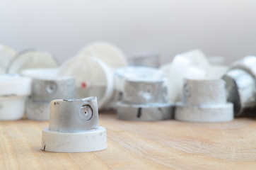 Several plastic nozzles from a paint sprayer that lie on a wooden surface against a gray wall background. The caps are smeared in chrome paint. The concept of street art and graffiti © mehaniq41