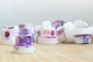 Several plastic nozzles from a paint sprayer that lie on a wooden surface against a gray wall background. The caps are smeared in violet paint. The concept of street art and graffiti © mehaniq41