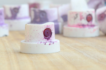 Several plastic nozzles from a paint sprayer that lie on a wooden surface against a gray wall background. The caps are smeared in violet paint. The concept of street art and graffiti © mehaniq41