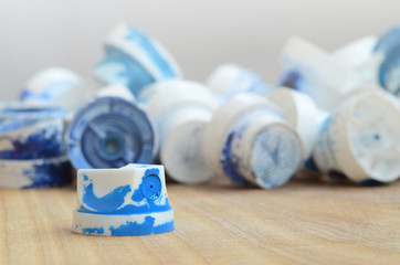 Several plastic nozzles from a paint sprayer that lie on a wooden surface against a gray wall background. The caps are smeared in blue paint. The concept of street art and graffiti © mehaniq41