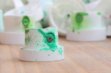 Several plastic nozzles from a paint sprayer that lie on a wooden surface against a gray wall background. The caps are smeared in green paint. The concept of street art and graffiti © mehaniq41