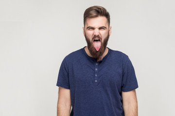 Obraz premium Crazy and fun concept. Bearded young adult man showing tongue