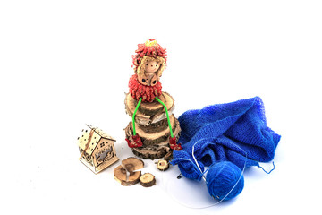 Fototapeta na wymiar Doll on wooden round logs, knitting yarns and a house