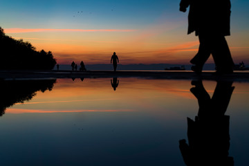 Fototapeta premium Reflections of People Silhouettes Walking by the Sea, against beautiful after sunset color tones