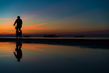 Silhuette of Man on Bicycle and his reflection on water from rain, against Lovely Colors Sky