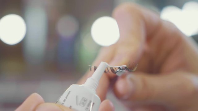 Makeup artist applying glue on the false eyelashes, closeup slow motion