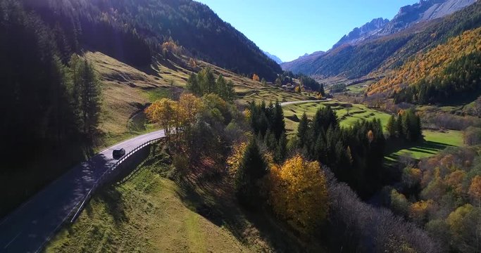Car on a autumn color road,  aerial view following cars driving between mountains, on a colorful fall alp road, on a sunny autumn day, on nufenen pass, in the swiss alps, in ticino, switzerland