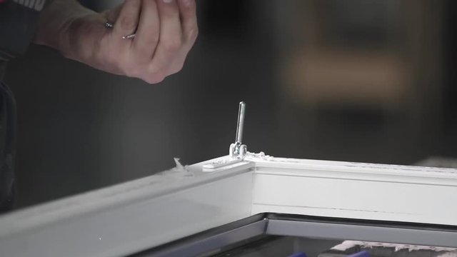 Manufacture of plastic windows and doors. Worker fastens the fittings with a screwdriver to the plastic window in the shop for the production of plastic and metal windows and doors. Screwing screws.