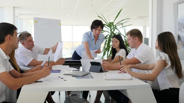 woman boss with documents in hand holding meet with Young collaborators behind big white table into modern boardroom