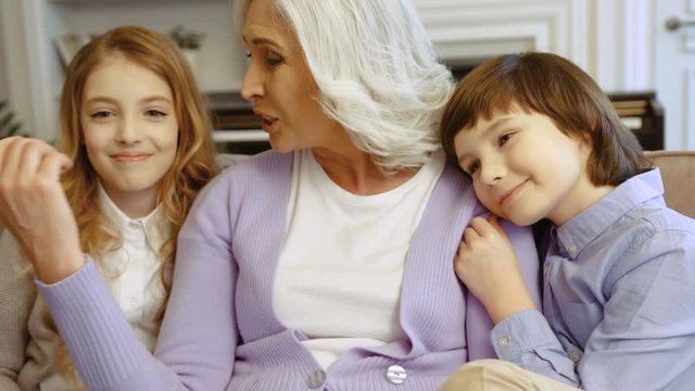 Portrait of grandmother and her grandchildren hugging while sitting on the sofa in the living room at home. Close up